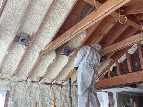 A spray foam installer working in a residential attic — a textbook example of where spray foam outperforms traditional insulation like fiberglass.