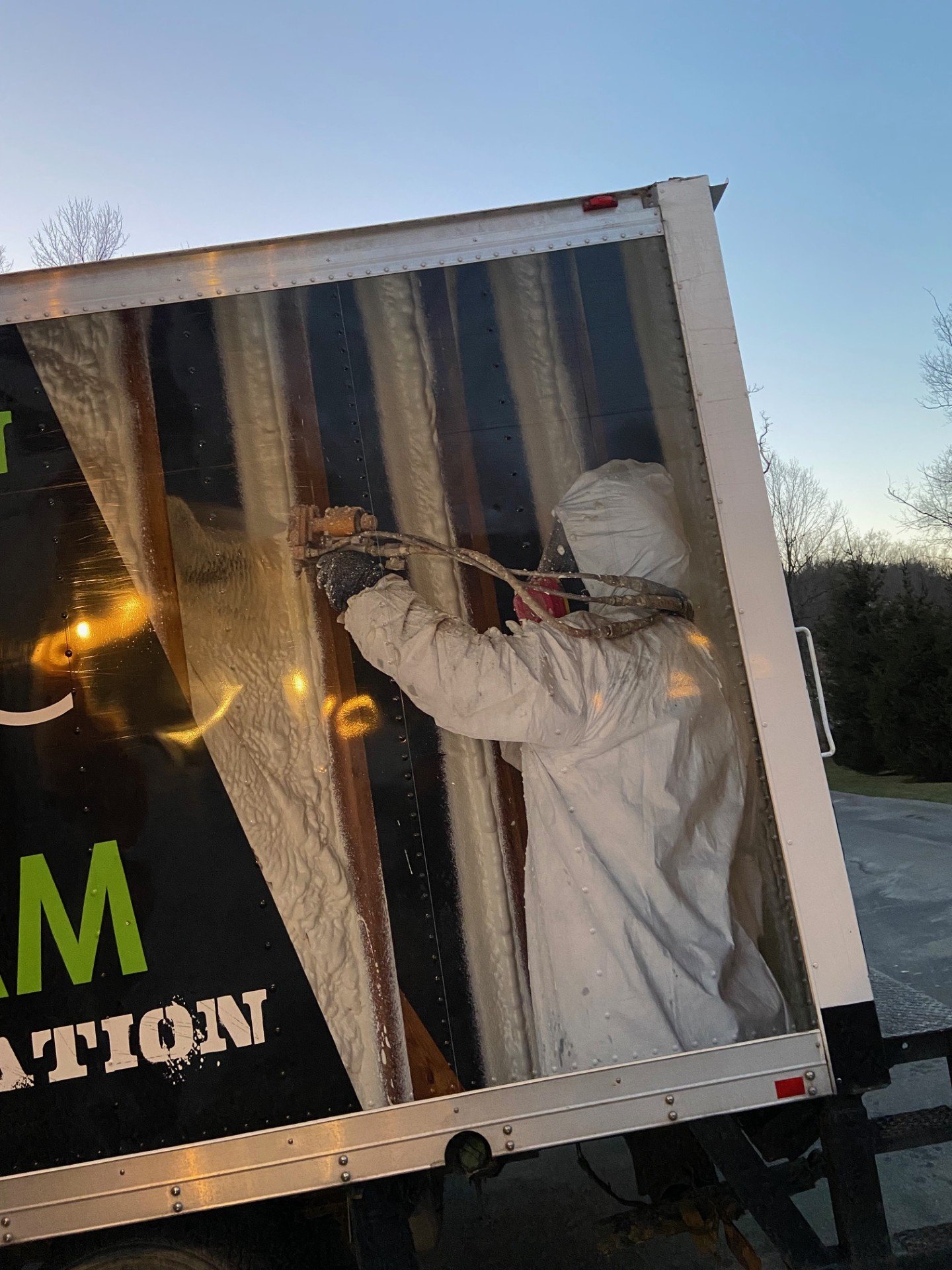 Liquid Green technician in protective suit spraying closed cell foam on trailer exterior